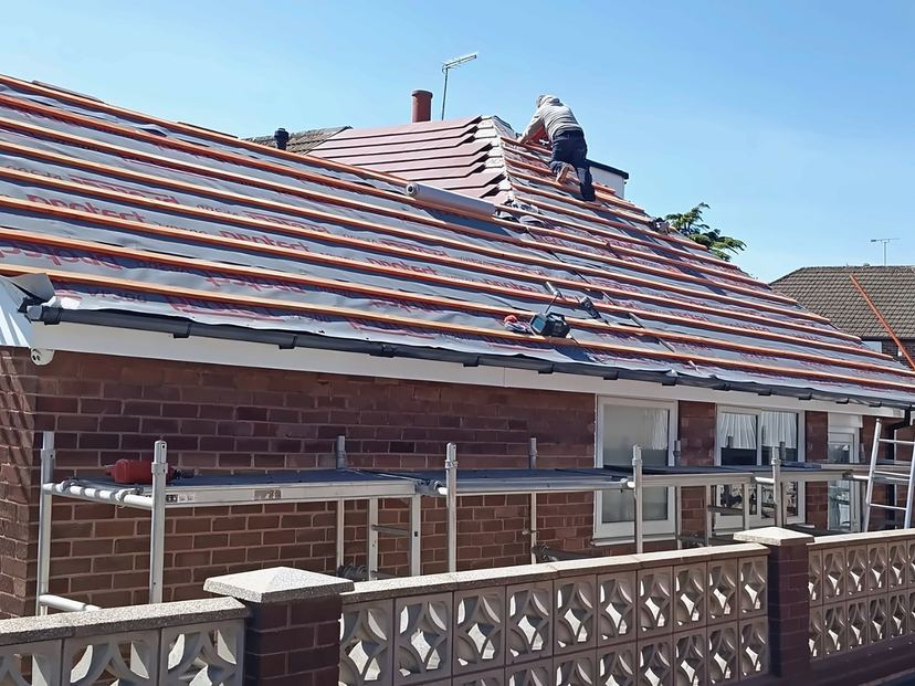 Re-roofing another bungalow: new battens, red tiles laid up to the hip, roofer at the top