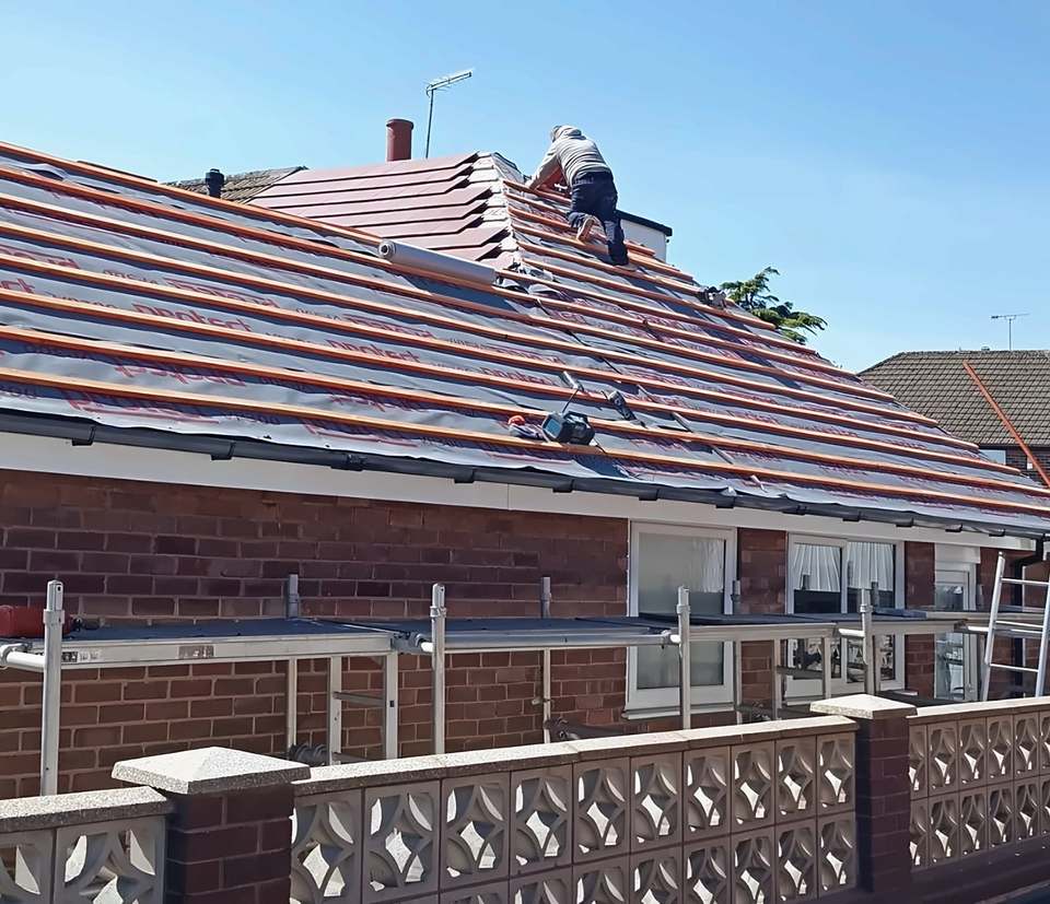 Re-roofing another bungalow: new battens, red tiles laid up to the hip, roofer at the top